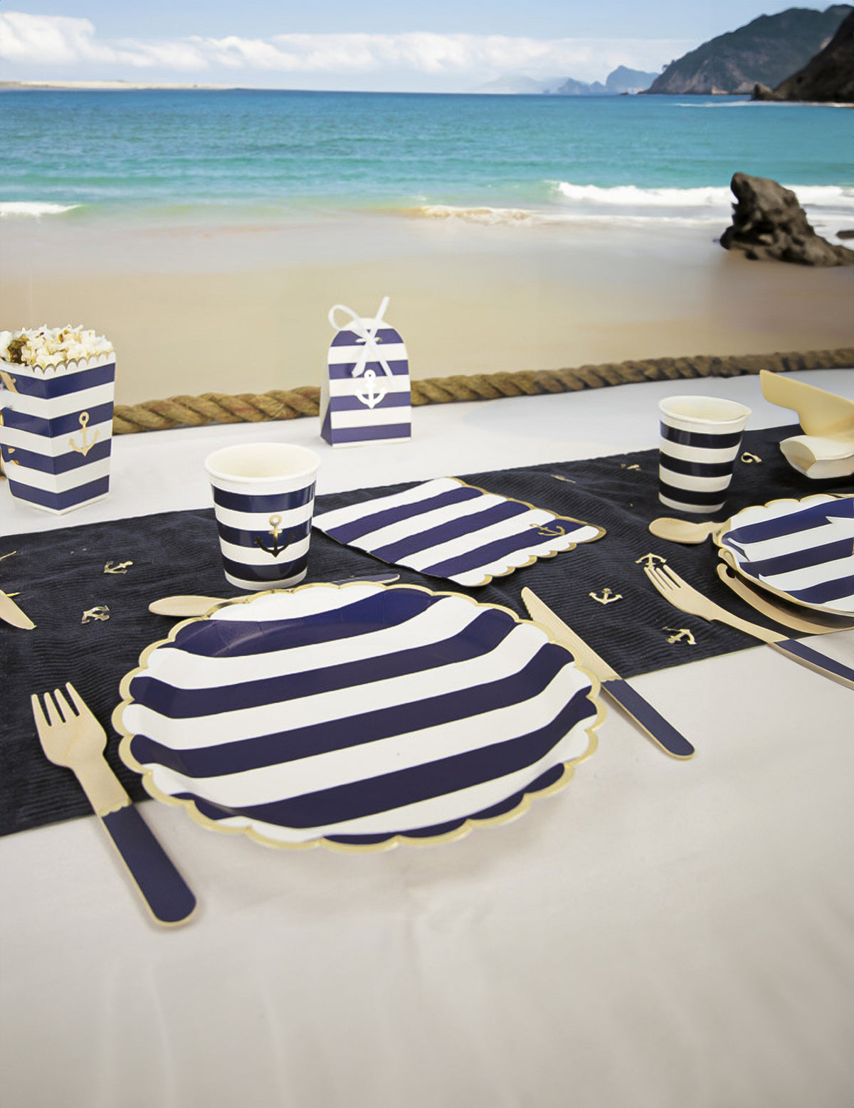 Mise en situation sur la plage des serviettes festonnées en papier marinière bleu marine et blanc à bords dorés avec ancre
