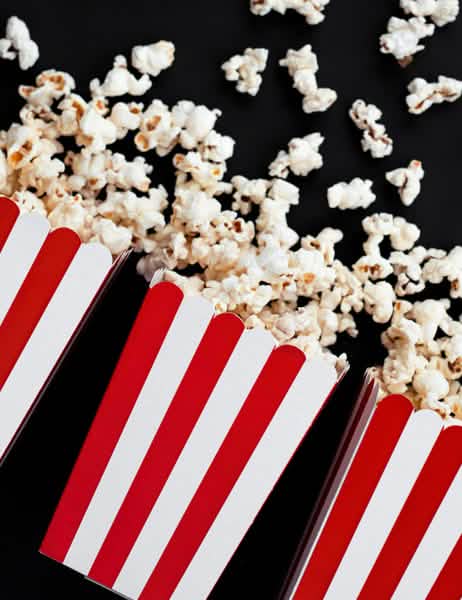 Kaatunutta popcornia punaisista ja valkoisista raidallisista pahvisista popcorn-laatikoista