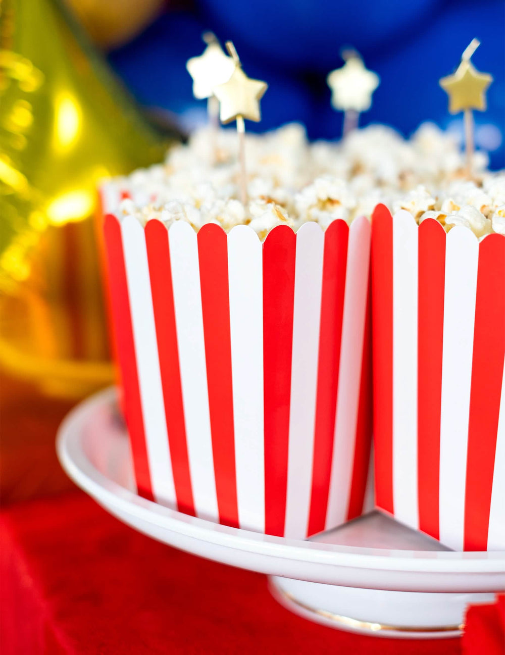 Lähikuva sisällöstä tähtikuvioisilla piikeillä varustetuista punavalkoraidallisista pahvisista popcorn-laatikoista juhliin