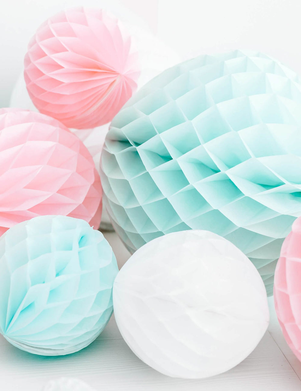 Mise en scène aux tons pastel de la boule en papier alvéolé pour déco de fête blanc